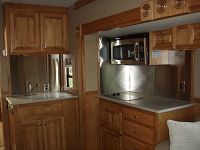 Kitchen in slideout w/stainless backsplash, microwave, 2-burner stove & storage areas